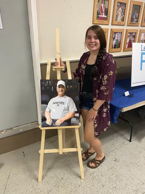 Rebekah Wiand standing with a painting she did of Leon Fultz.